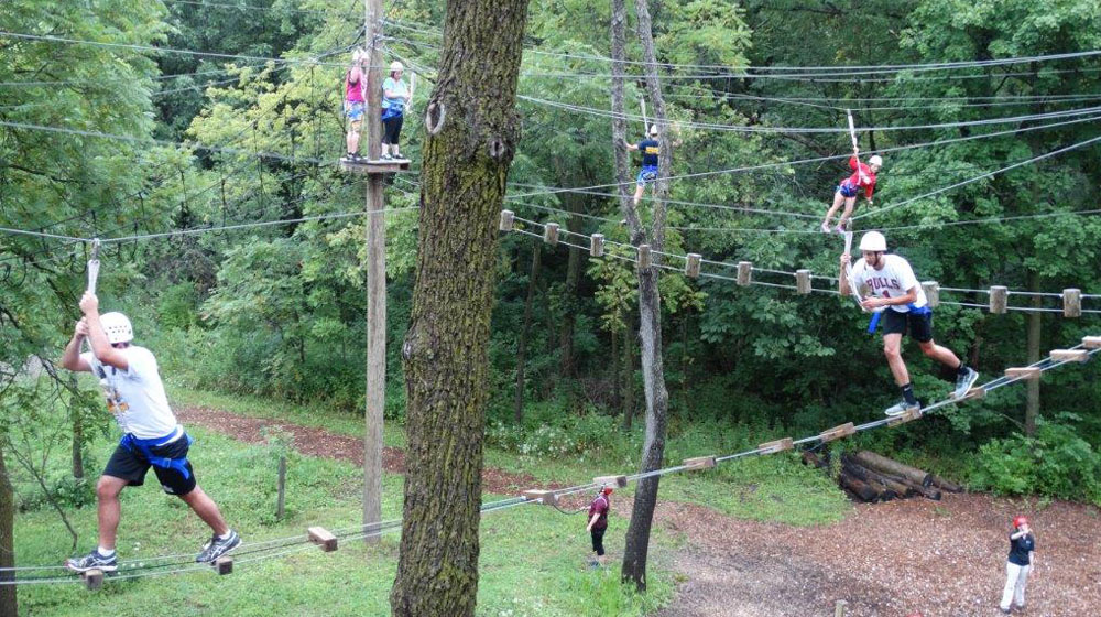 Multiple people are suspended high above the ground as they traverse a ropes course